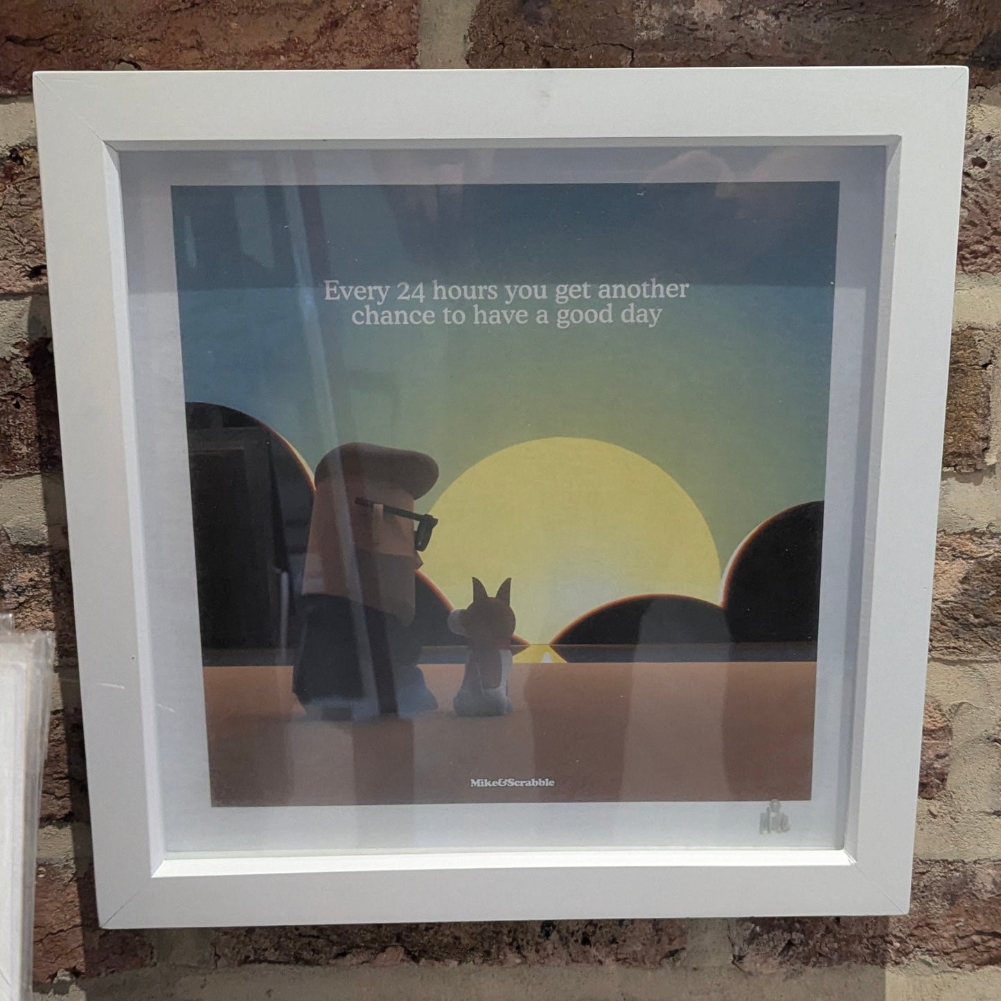 Framed artwork with a sunset scene and motivational quote on a stone wall.